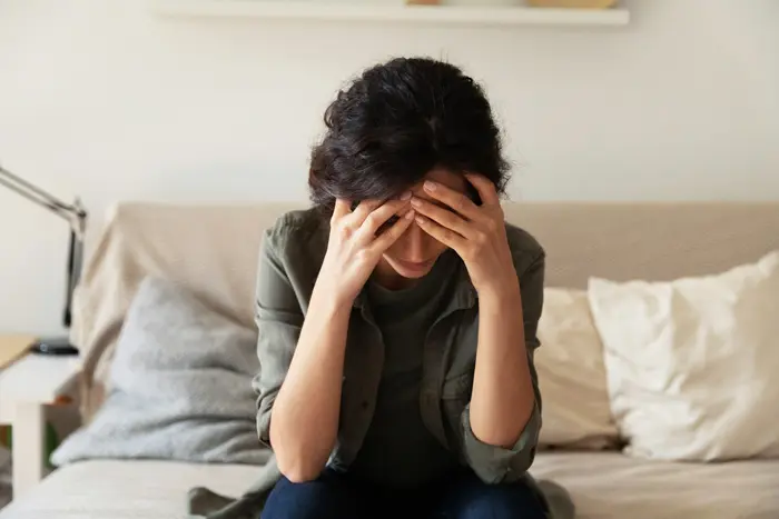 woman sitting on bed with her head in her hands - signs of substance use disorder