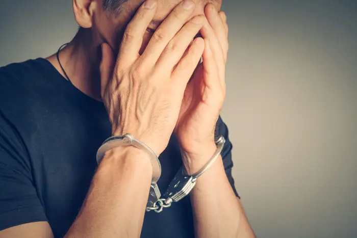 closely cropped shot of handcuffed man holding his hands up to his face in shame or remorse - incarceration and addiction