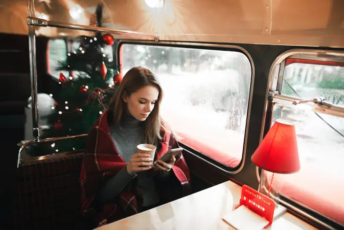 woman sitting in cozy cafe during the holidays using her phone - sober fun