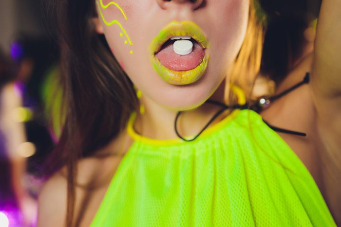 closeup shot of woman dressed in neon green with a tab of ecstasy on her tongue