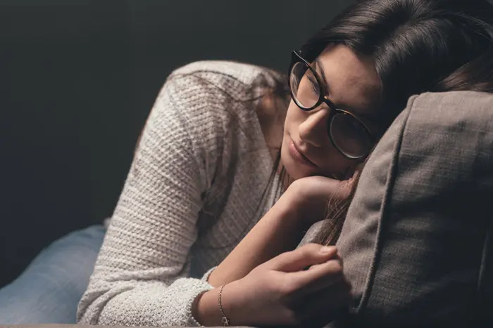 young woman in glasses curled up on a chair or couch, looking sad - separation anxiety, codependency 