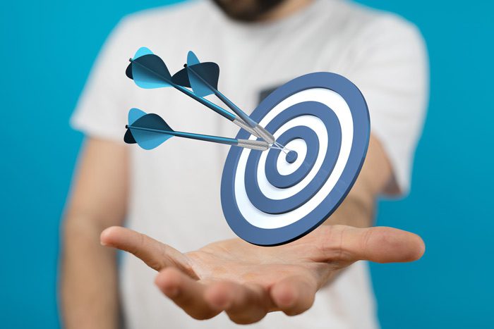 cropped shot of man's arm and chest holding out a bullseye target with arrows in it - goal-setting