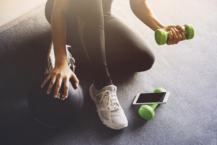 Holistic Therapies; cropped shot of bottom half of a woman using dumb bells and cell phone - holistic therapies