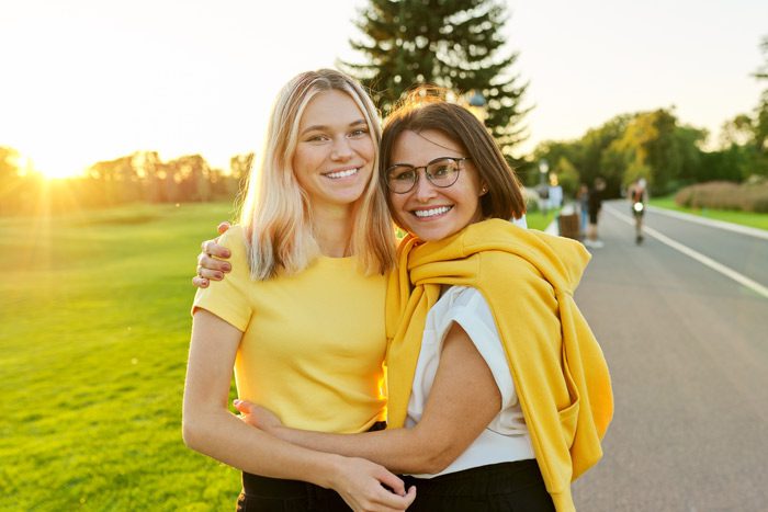 beautiful mom and teen daughter both wearing yellow and side-hugging while smiling at the camera