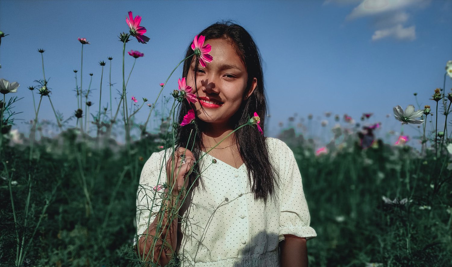 Smiling Asian woman holding stems of flowers on nature
