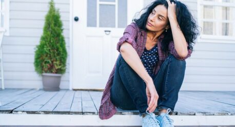 Sad mid adult woman sitting on stairs in front of her house